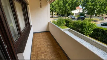 Heller Balkon mit Holzbodenfliesen und Blick ins Grüne, ideal für entspannte Stunden im Freien.