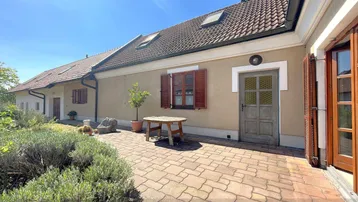 Sonniger Außenbereich mit gepflasterter Terrasse, umgeben von mediterranen Pflanzen und einem Holztisch.