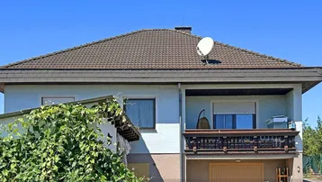 Ansicht des Hauses mit Satteldach, Balkon und integrierter Garage im Erdgeschoss.