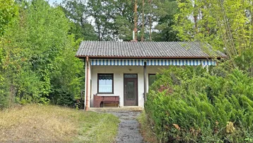 Kleines Haus umgeben von üppiger Vegetation und Bäumen in ländlicher Umgebung.