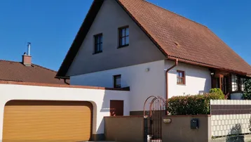 Ansicht des Einfamilienhauses von vorne mit Satteldach und integrierter Garage unter blauem Himmel.