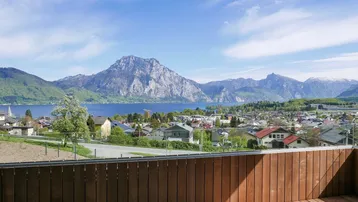 Geräumiger Balkon mit Holzboden und einem weiten, sonnigen Blick auf den See und die umliegende Berglandschaft.