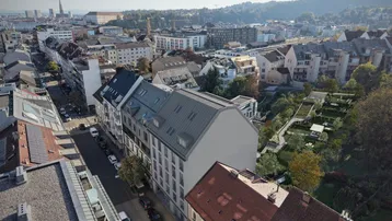 Panoramablick über eine städtische Umgebung mit Wohngebäuden und grünen Hügeln im Hintergrund.