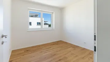 Helles Schlafzimmer mit Holzboden und großem Fenster, das viel Tageslicht hereinlässt.