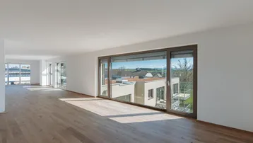 Geräumiger, lichtdurchfluteter Wohnbereich mit breiten Fenstern und Holzboden, bietet einen weiten Ausblick.