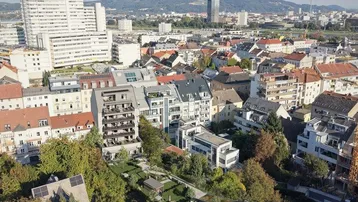 Weitläufiger Blick über eine Stadtlandschaft mit Gebäuden und Bergen am Horizont.