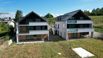 Zwei moderne Neubauten mit Satteldach und großen Fensterfronten in ländlicher Umgebung.