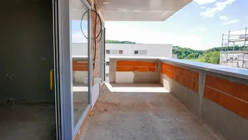 Unfertiger Balkon mit Betonboden und Ziegelwänden, bereit für den Ausbau in einem Neubauprojekt.