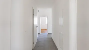 Heller Flur mit weißen Wänden und grauen Fliesen, der zu weiteren Zimmern mit Holzboden führt.