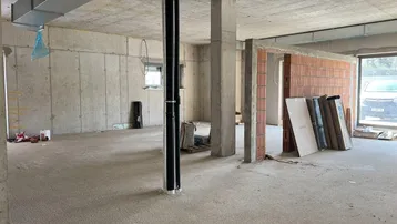 Rohbau eines großen Raumes mit Betonwänden, Säulen und sichtbaren Lüftungsrohren.