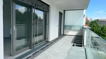 Geräumiger Balkon im Bau mit Fliesenboden und Glasgeländer, bereit für die Fertigstellung.