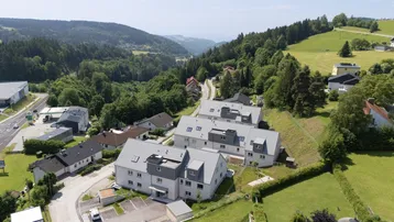 Panoramablick auf die Wohnanlage in einem grünen Tal, umgeben von Wäldern und Hügeln.