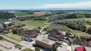 Luftaufnahme einer ländlichen Gegend mit Wohngebäuden, Feldern und Bergen im Hintergrund.