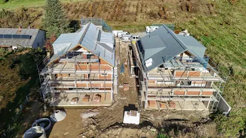 Zwei im Bau befindliche Häuser mit Gerüsten und teilweise gedeckten Dächern in ländlicher Umgebung.