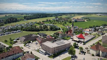 Luftaufnahme einer ländlichen Umgebung mit einem modernen Gebäude im Zentrum und Bergen im Hintergrund.