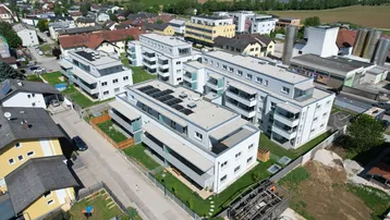 Luftaufnahme einer modernen Wohnanlage mit mehreren Gebäuden, Grünflächen und Photovoltaikanlagen auf den Dächern.