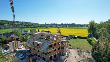Luftaufnahme eines im Bau befindlichen Gebäudes mit Kran und umliegenden Feldern.