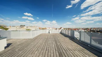Große Dachterrasse mit Holzbelag und weitem Blick über die Stadt unter blauem Himmel.