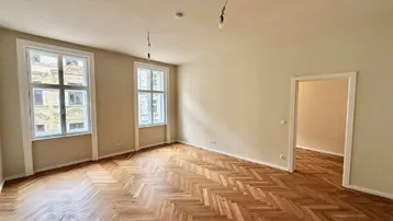Geräumiges Wohnzimmer mit Fischgrätparkett und hohen Fenstern, bereit für die Einrichtung.