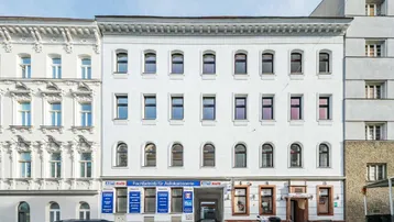 Die weiße Fassade des Mehrfamilienhauses mit vielen Fenstern und Geschäften im Erdgeschoss.