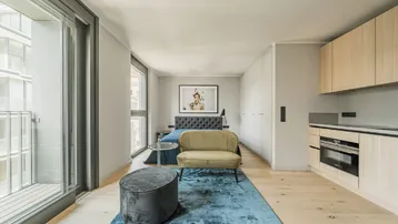 Modernes Studio-Apartment mit integrierter Küchenzeile, Holzboden und Zugang zum Balkon.