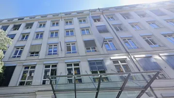 Ansicht der modernen Gebäudefassade mit zahlreichen Fenstern, Jalousien und einem eleganten Glasvordach über dem Eingang.