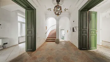 Historischer Eingangsbereich mit hohen Decken, Stuckverzierungen und grünen Flügeltüren.