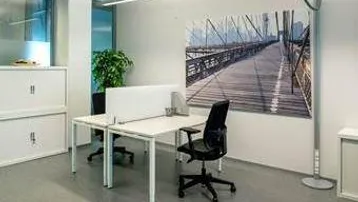 Helles und modernes Büro mit zwei Arbeitsplätzen, weißen Schränken und einem großen Fenster, das viel Tageslicht hereinlässt.