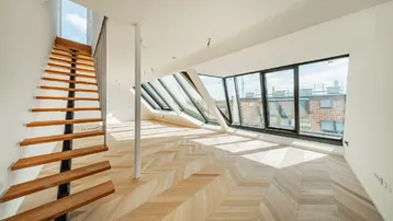 Heller Wohnbereich mit Fischgrätparkett, großen Dachfenstern und moderner Treppe.
