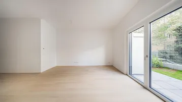 Helles, leeres Zimmer mit hellem Parkettboden und Zugang zu einer Terrasse oder einem Garten.