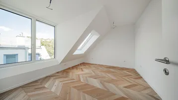Helles Dachzimmer mit modernem Fischgrätparkett, großen Fenstern und Dachschräge.