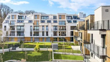 Moderne Wohngebäude mit weißer Fassade, Holzverkleidung und begrünten Außenanlagen unter blauem Himmel.