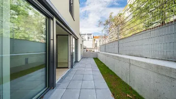 Gepflasterte Terrasse mit Zugang zu den Innenräumen und einer kleinen Rasenfläche.