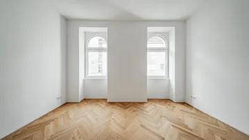Helles Zimmer mit Fischgrätparkett und zwei Rundbogenfenstern, bereit zur individuellen Gestaltung.