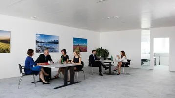 Heller und moderner Büroraum mit mehreren Besprechungstischen und schlichtem Design.