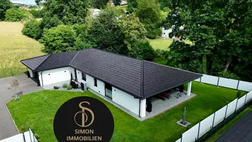 Luftaufnahme eines modernen Einfamilienhauses mit dunklem Dach und gepflegtem Garten in ländlicher Umgebung.