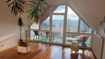 Helles Wohnzimmer im Dachgeschoss mit großen Fenstern und Panoramablick auf die Landschaft.