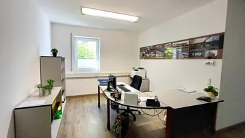 Geräumiges Büro mit modernem Schreibtisch, Holzfußboden und Blick ins Grüne durch das Fenster.