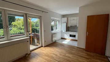 Heller Wohnbereich mit Parkettboden, Zugang zum Balkon und integrierter Küchenzeile.