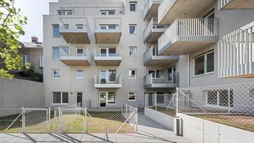 Modernes Mehrfamilienhaus mit mehreren Balkonen und einem kleinen Grünbereich im Vordergrund.