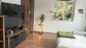 Helles Wohnzimmer mit Laminatboden, modernen Möbeln und Blick ins Grüne durch das Fenster.