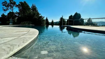 Nahaufnahme des eleganten Infinity-Pools mit Steinumrandung, der nahtlos in die Landschaft übergeht.