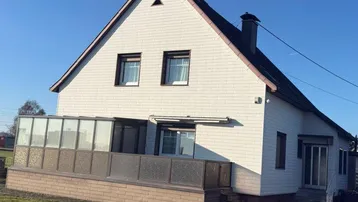 Freistehendes Einfamilienhaus mit Satteldach und einem verglasten Wintergarten im Erdgeschoss.
