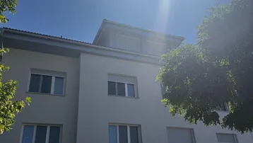 Fassade eines modernen Mehrfamilienhauses mit Tiefgaragenzufahrt unter strahlendem Sonnenschein.