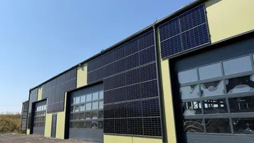 Gebäudefassade mit mehreren Garagentoren und Photovoltaik-Modulen für nachhaltige Energiegewinnung.
