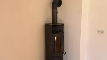 Gemütlicher Wohnbereich mit modernem Holzofen und Parkettboden in einer Ecke des Zimmers.