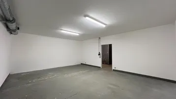 Geräumiger, leerer Lagerraum mit Betonboden und sichtbaren Rohren an der Decke und Wänden.