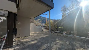 Blick auf den Neubau von unten mit Balkon und sonniger Bergkulisse während der Bauphase.