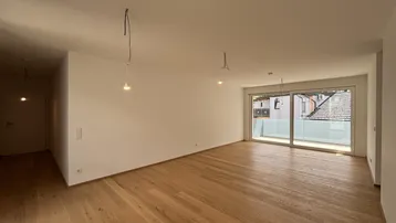Helles, leeres Wohnzimmer mit neuem Holzparkettboden und Zugang zu einem Balkon.