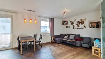 Geräumiger Wohn-Essbereich mit Holzboden und Fliesen, gemütlicher Sitzecke und Zugang zum Balkon.